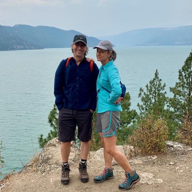 Deb and Steve standing at rest on a hiking trail in British Columbia. A lake and mountains are visible behind them.